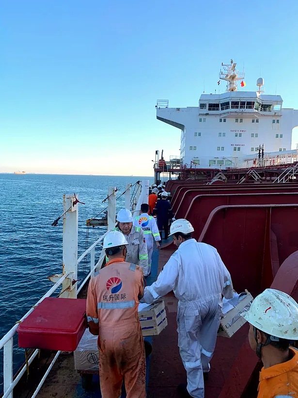 Crew members carrying supply crates along a ship deck at sea